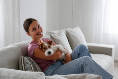 Genç ve güzel bir kadının portresi. Kanepede uzanmış. Tel saçlı Jack Russel teriyeri köpeğiyle. Sert kaplamalı sevimli kız eğleniyor. Arkaplan, kapat, boşluğu kopyala.
