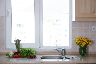 Lavabonun yanındaki pencerenin altındaki mermer mutfak tezgahında yığınla farklı organik meyve, sebze ve sebze yığını var. Kapat, metin, arkaplan ve üst görünüm için boşluk kopyala.