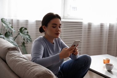 Yüzünde konsantre bir ifade olan esmer kadının portresi kanepede oturmuş telefonda yazıyor. Neşeli kadın bir video görüşmesi yapıyor. Arkaplan, kopyala boşluk, kapat.