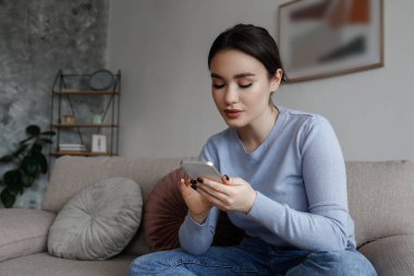 Yüzünde konsantre bir ifade olan esmer kadının portresi kanepede oturmuş telefonda yazıyor. Neşeli kadın bir video görüşmesi yapıyor. Arkaplan, kopyala boşluk, kapat.