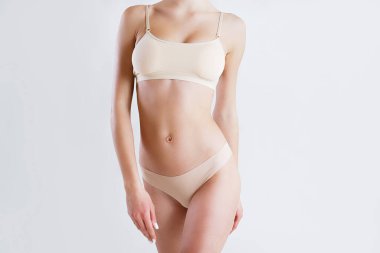 Beyaz arka planda izole edilmiş iç çamaşırlı, tanınmayan fit bir kadını yakından çek. Düz göbekli, bej iç çamaşırlı, zayıf, çekici bir kadın gövdesi. Metin için alanı kopyala.