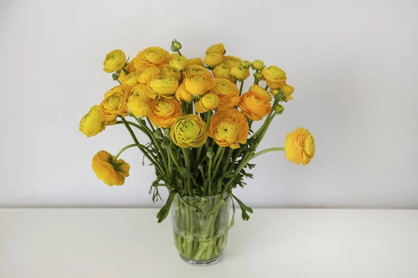 テーブルの上のガラス花瓶に美しい柔らかい黄色のオレンジのランキュラスの花束 花弁の構造が見える 花芽の明るいパターン トップビュー 閉じる コピースペース 白い壁の背景 — ストック写真
