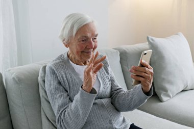 Yaşlı ve mutlu bir kadının torunlarıyla eğlenceli bir video görüşmesi görüntüsü. Öndeki kameraya gülümseyen bir telefon tutan yaşlı bayan. Arkaplan, kapat, boşluğu kopyala.