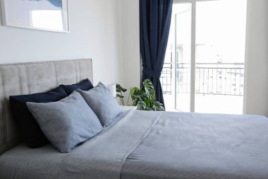 Yatak başlıklı, yeni yapılmış kral yataklı, temiz ve ütülenmiş çarşaflı, güneş ışığında şişkin yastıklı bir otel odası. Mobilya galerisinde büyük boy yatak. Kapat, metin için boşluk kopyala.