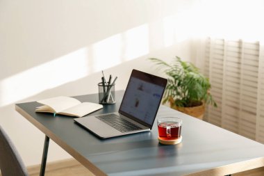 Merkez ofis konsepti. Pencerenin yakınındaki ev bölgesinden atanmış bir iş. Bulanık ekran ve cam çay kaplı modern bir laptop. Kapat, kopyala alanı, iç arkaplan.