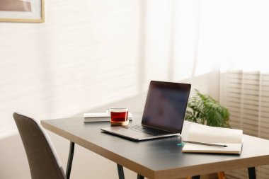 Merkez ofis konsepti. Pencerenin yakınındaki ev bölgesinden atanmış bir iş. Bulanık ekran ve cam çay kaplı modern bir laptop. Kapat, kopyala alanı, iç arkaplan.