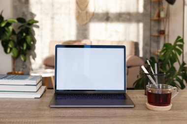 Boş ekran laptop, cep telefonu ve ahşap masada bir fincan. Doğal güneş ışığıyla dolu ev bitkileriyle dolu rahat bir ofis. Kapat, kopyala boşluk, arkaplan.