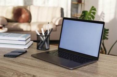 Blank screen laptop, cell phone and a cup on wooden table. Cozy lofty office with house plants full of natural sunlight. Close up, copy space, background.