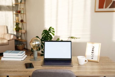 Boş ekran laptop, cep telefonu ve ahşap masada bir fincan. Doğal güneş ışığıyla dolu ev bitkileriyle dolu rahat bir ofis. Kapat, kopyala boşluk, arkaplan.
