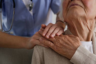 Unrecognizable female doctor expressing care towards an elderly lady, comforting her and holding hands. Two adult women of different age. Family values concept. lose up, copy space, background.