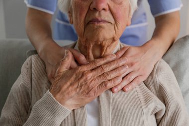 Unrecognizable female doctor expressing care towards an elderly lady, hugging her from behind holding hands. Two adult women of different age. Family values concept. lose up, copy space, background.
