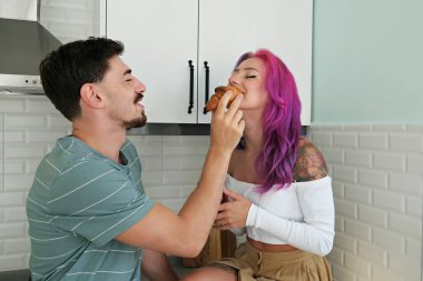 Sevgi dolu çift mutfakta eğleniyor. Sakallı adam ve parlak renkli saçlı kız arkadaşı evde Fransız kruvasanı yiyorlar. Kapat, kopyala boşluk, arkaplan.