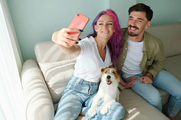 Happy hipster couple with their rough coated dog. Young woman with pink purple hair and her bearded boyfriend taking a selfie with wire haired jack russell terrier. Close up, copy space, background.