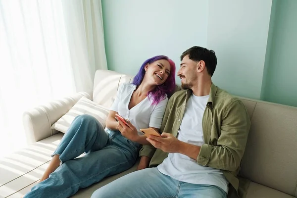 Hipster Couple Sitting Couch Exchanging Memes Phones Home Young Woman — Fotografia de Stock