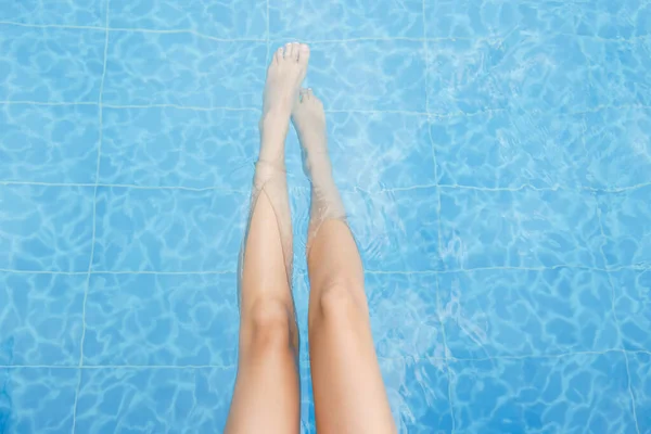 Cropped shot of a young woman dipping her feet in the pool water. Unrecognizable female relaxing by the pool, cooling down. Background, copy space, close up