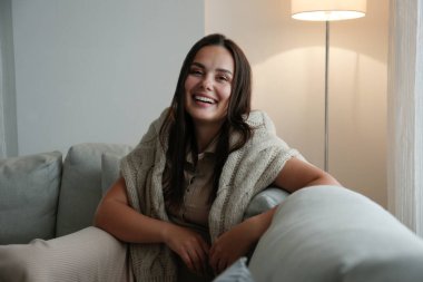 Uzun düz esmer saçlı güzel bir kadının portresi kanepede oturuyor ve gülümsüyor. Kahverengi gözlü kadının mükemmel gülüşünü yakından çek. Boşluğu kopyala, arkaplan.