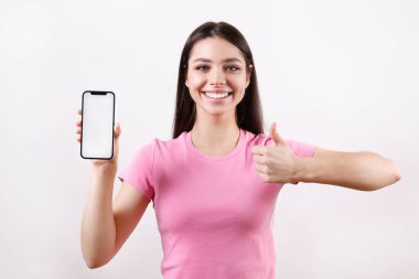 Young beautiful brunette woman wearing pink t-shirt posing with a phone over isolated white background. Portrait of female model showing blank screen cellphone. Close up, copy space.