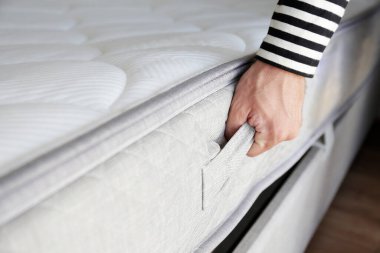 Yeni yatak teslimatı ve montaj hizmeti konsepti. Ortopedik köpük yatağı müşterinin yatak odasındaki leşin üzerine sererken erkek işçinin ellerinin kırpılmış görüntüsü. Kapat, kopyala boşluk, arkaplan.