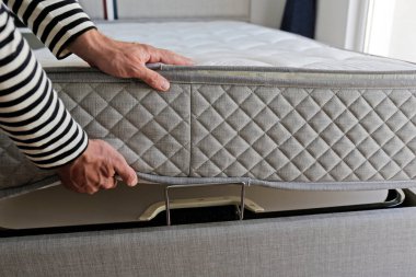 Yeni yatak teslimatı ve montaj hizmeti konsepti. Ortopedik köpük yatağı müşterinin yatak odasındaki leşin üzerine sererken erkek işçinin ellerinin kırpılmış görüntüsü. Kapat, kopyala boşluk, arkaplan.