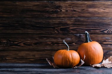 Thanksgiving background concept. Local produce pumpkin and autumn maple leaves as traditional autumnal holidays decoration on a dark wood table. Close up, copy space for text, top view, flat lay.
