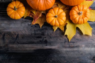 Thanksgiving background concept. Local produce pumpkin and autumn maple leaves as traditional autumnal holidays decoration on a dark wood table. Close up, copy space for text, top view, flat lay.