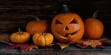 Big orange pumpkin carved into Jack o Lantern and a bunch of small ones on dark wood textured table. All hallows eve Halloween party decoration concept. Background, copy space, close up, top view.