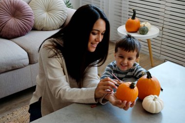 Üç yaşındaki oğluyla birlikte evde cadılar bayramı için dekorasyon hazırlıyorlardı. Kadın çocuğuyla güzel vakit geçiriyor, balkabağı oyuyor. Kapat, kopyala boşluk, arkaplan.