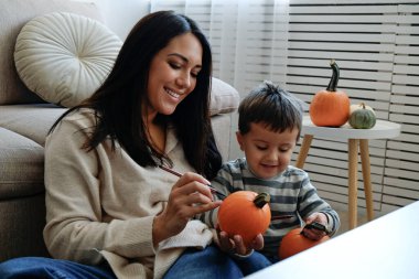 Üç yaşındaki oğluyla birlikte evde cadılar bayramı için dekorasyon hazırlıyorlardı. Kadın çocuğuyla güzel vakit geçiriyor, balkabağı oyuyor. Kapat, kopyala boşluk, arkaplan.