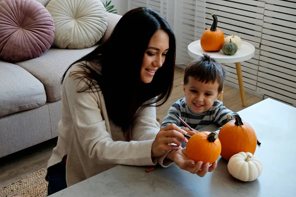 Üç yaşındaki oğluyla birlikte evde cadılar bayramı için dekorasyon hazırlıyorlardı. Kadın çocuğuyla güzel vakit geçiriyor, balkabağı oyuyor. Kapat, kopyala boşluk, arkaplan.