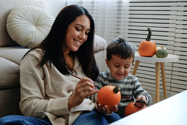 Üç yaşındaki oğluyla birlikte evde cadılar bayramı için dekorasyon hazırlıyorlardı. Kadın çocuğuyla güzel vakit geçiriyor, balkabağı oyuyor. Kapat, kopyala boşluk, arkaplan.
