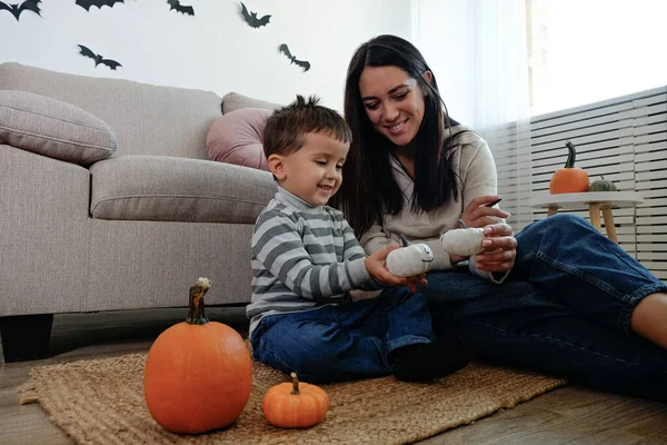 Young beautiful woman with her three year old son preparing decorations for halloween at home. Mom spending quality time with her child, messing around with pumpkins. Close up, copy space, background.