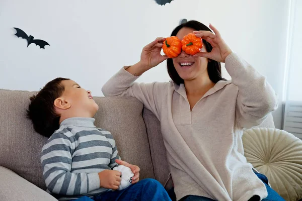 Young beautiful woman with her three year old son preparing decorations for halloween at home. Mom spending quality time with her child, messing around with pumpkins. Close up, copy space, background.