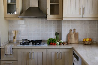 Close up shot of kitchen with classic style interior. Wooden furniture, gas cooktop, eco friendly bamboo kitchen utensil, cutting board and fresh vegetables on marble tabletop. Copy space, background.
