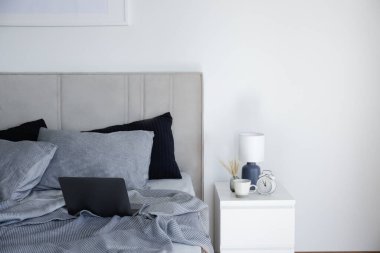 Laptop on a king sized bed with headboard, perfectly clean and ironed sheets, puffy pillows in natural sun light. Empty bed with a computer. Close up, copy space for text.