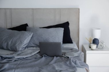 Laptop on a king sized bed with headboard, perfectly clean and ironed sheets, puffy pillows in natural sun light. Empty bed with a computer. Close up, copy space for text.