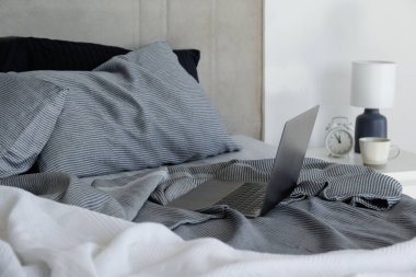 Laptop on a king sized bed with headboard, perfectly clean and ironed sheets, puffy pillows in natural sun light. Empty bed with a computer. Close up, copy space for text.