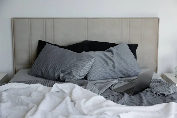 Laptop on a king sized bed with headboard, perfectly clean and ironed sheets, puffy pillows in natural sun light. Empty bed with a computer. Close up, copy space for text.