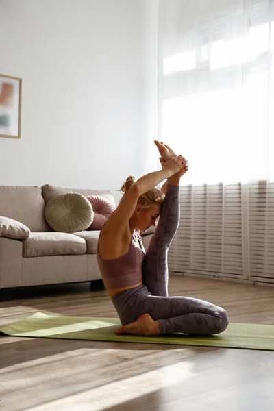 Sporty adult woman practicing yoga, doing one leg raised to head pose. Fit middle aged yogini performing morning physical exercise routine at the living room. Interior background, copy space, close up