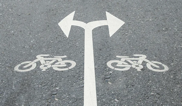 Белая стрелка поворачивает налево и поворачивает направо с велосипедным знаком на дороге f — стоковое фото