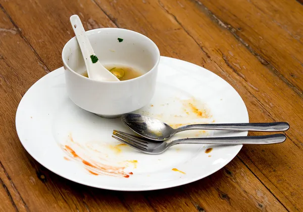 Грязная тарелка с ложкой и вилкой на деревянном столе — стоковое фото