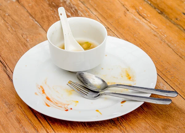 Dirty plate with spoon and fork on wood table — Stock Photo, Image