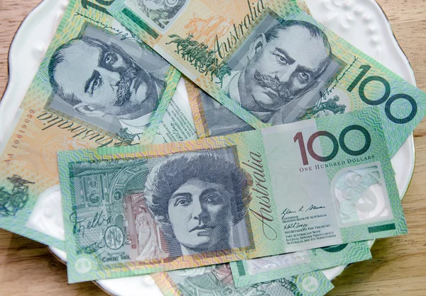 Barevné australské měny na bílé plotně na dřevěný stůl — Stock fotografie