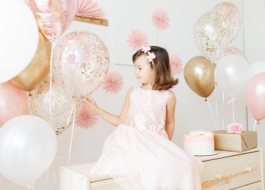 Altı yaşında açık pembe elbiseli bir kız evde doğum gününü kutluyor..