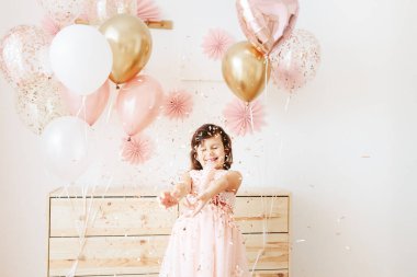 Altı yaşında açık pembe elbiseli bir kız evde doğum gününü kutluyor..