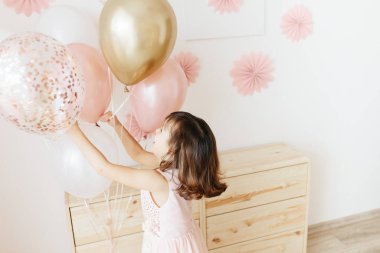 Altı yaşında açık pembe elbiseli bir kız evde doğum gününü kutluyor..