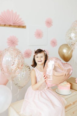 Altı yaşında açık pembe elbiseli bir kız evde doğum gününü kutluyor..