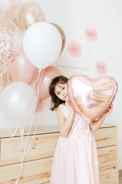 Altı yaşında açık pembe elbiseli bir kız evde doğum gününü kutluyor..