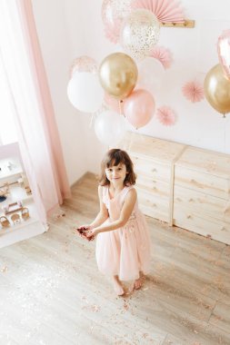 Altı yaşında açık pembe elbiseli bir kız evde doğum gününü kutluyor..