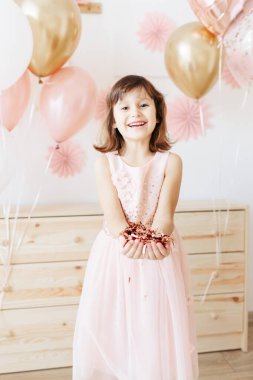 Altı yaşında açık pembe elbiseli bir kız evde doğum gününü kutluyor..