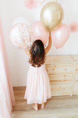 Altı yaşında açık pembe elbiseli bir kız evde doğum gününü kutluyor..